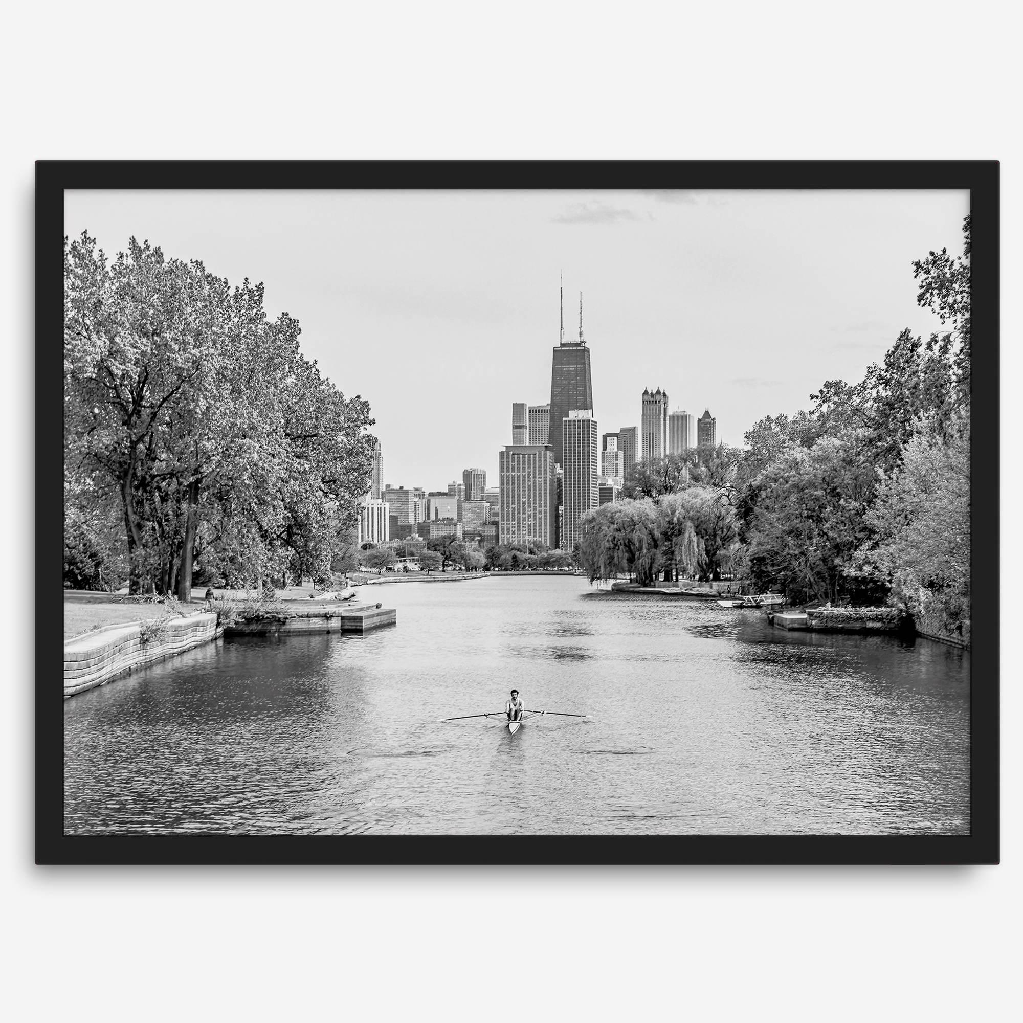 Black and white photo of Lincoln Park, Chicago. A lone rower glides on the park canal with the iconic Willis Tower (formerly Sears Tower) and Chicago skyline in the background.