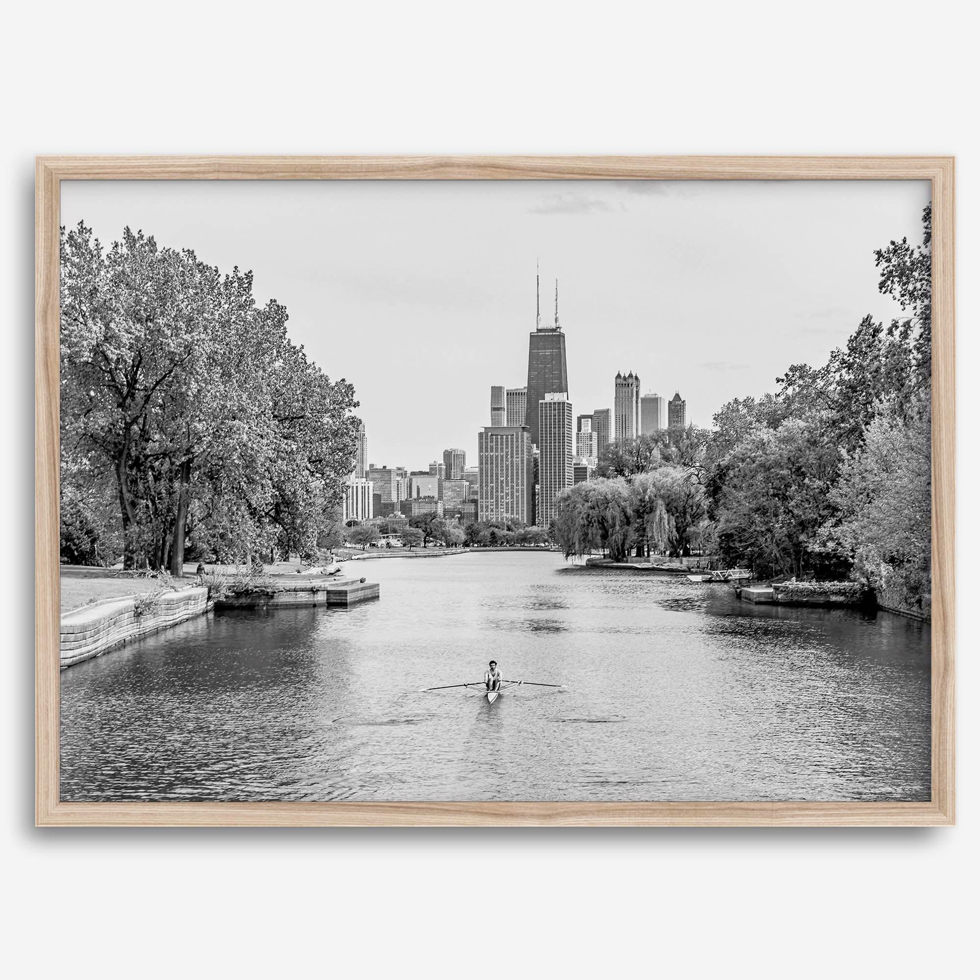 Black and white photo of Lincoln Park, Chicago. A lone rower glides on the park canal with the iconic Willis Tower (formerly Sears Tower) and Chicago skyline in the background.