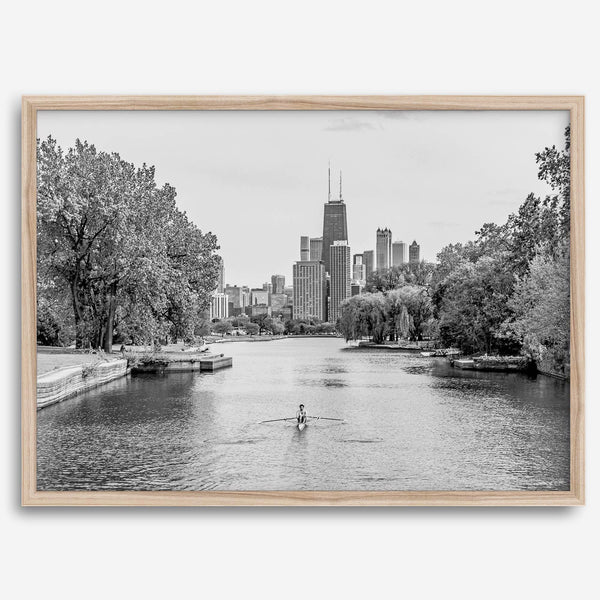 Black and white photo of Lincoln Park, Chicago. A lone rower glides on the park canal with the iconic Willis Tower (formerly Sears Tower) and Chicago skyline in the background.