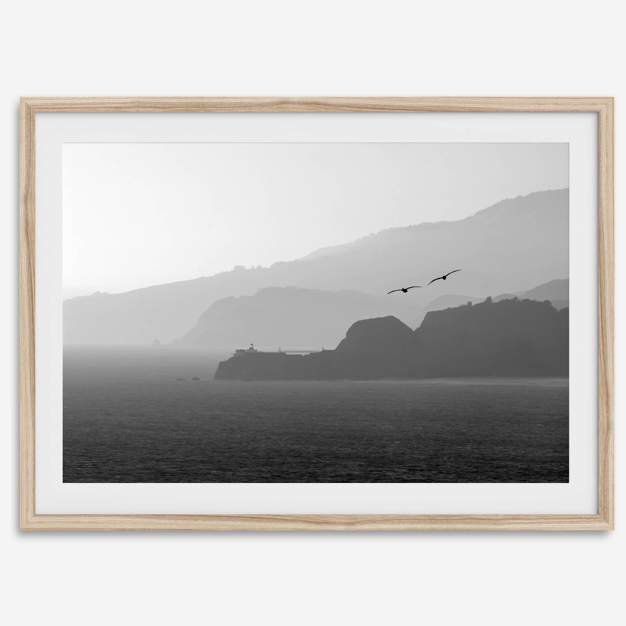 A black and white coastal wall art that showcases two Pelicans flying over the Pacific Ocean near the Golden Gate Bridge toward the layered mountains in the sunset.