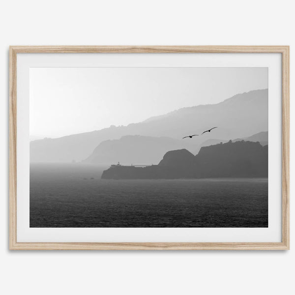 A black and white coastal wall art that showcases two Pelicans flying over the Pacific Ocean near the Golden Gate Bridge toward the layered mountains in the sunset.