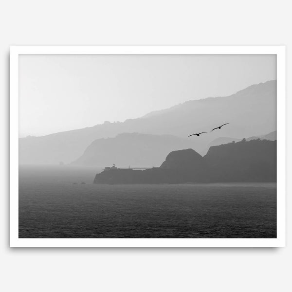 A black and white coastal wall art that showcases two Pelicans flying over the Pacific Ocean near the Golden Gate Bridge toward the layered mountains in the sunset.
