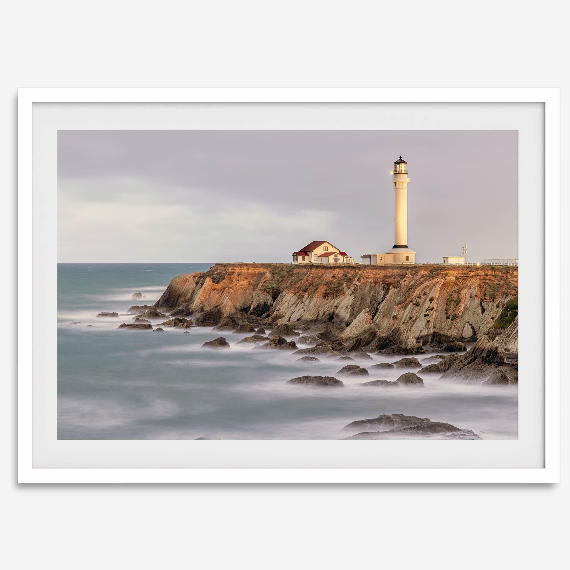 Long exposure fine art photography print of Pigeon Point Lighthouse at sunset. Golden light illuminates the lighthouse and cliffs, while the ocean surf crashes against the rocks in a creamy blur.
