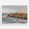 Long exposure fine art photography print of Pigeon Point Lighthouse at sunset. Golden light illuminates the lighthouse and cliffs, while the ocean surf crashes against the rocks in a creamy blur.