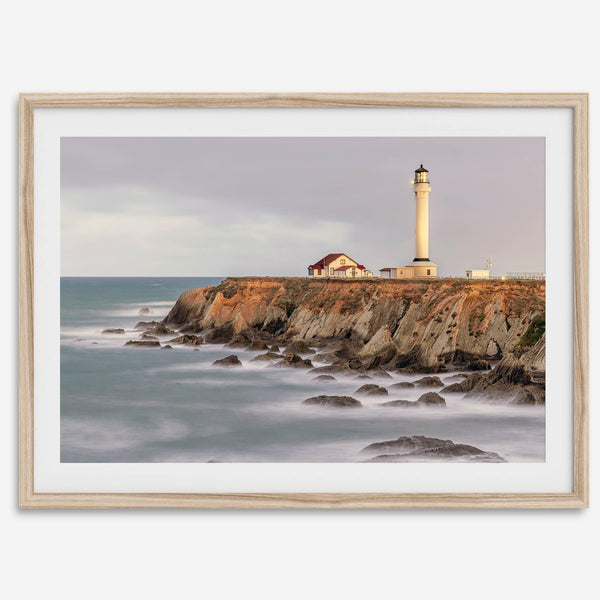 Long exposure fine art photography print of Pigeon Point Lighthouse at sunset. Golden light illuminates the lighthouse and cliffs, while the ocean surf crashes against the rocks in a creamy blur.
