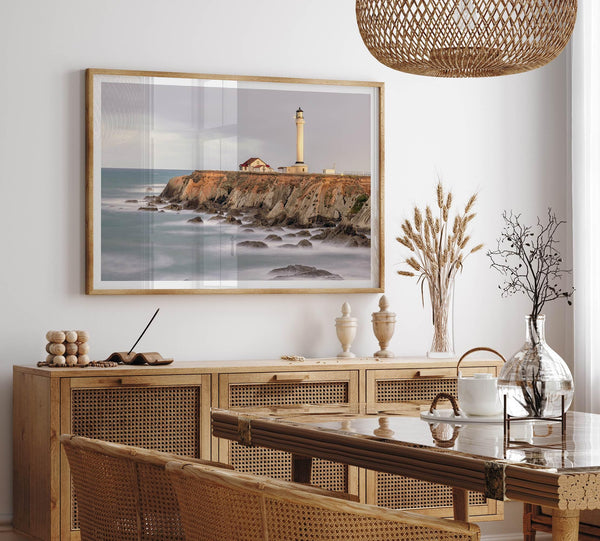 Long exposure fine art photography print of Pigeon Point Lighthouse at sunset. Golden light illuminates the lighthouse and cliffs, while the ocean surf crashes against the rocks in a creamy blur.