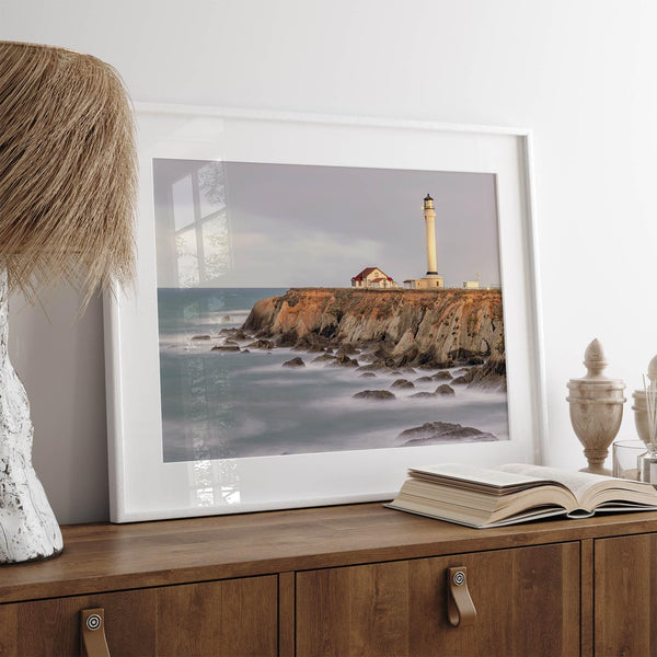 Long exposure fine art photography print of Pigeon Point Lighthouse at sunset. Golden light illuminates the lighthouse and cliffs, while the ocean surf crashes against the rocks in a creamy blur.