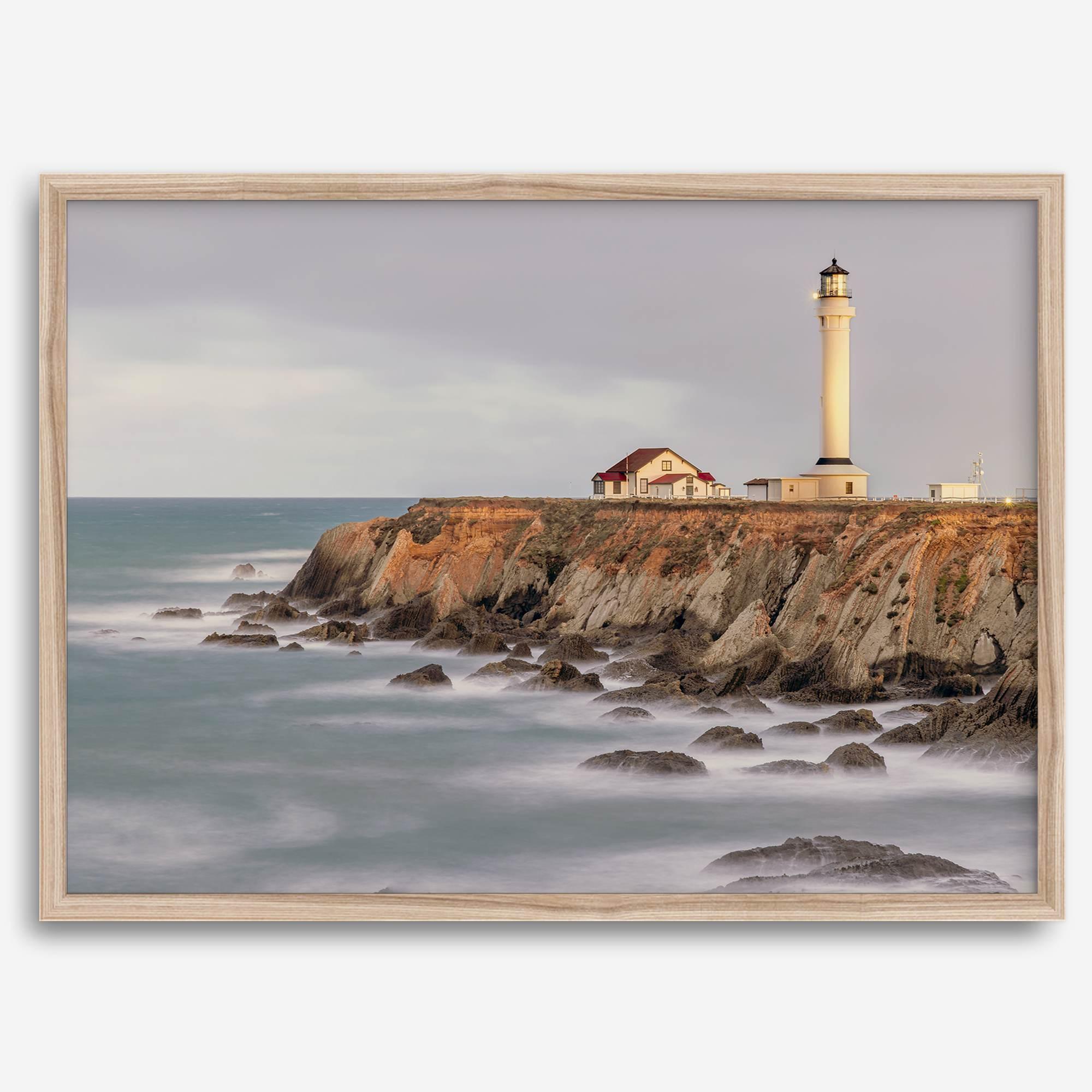 Long exposure fine art photography print of Pigeon Point Lighthouse at sunset. Golden light illuminates the lighthouse and cliffs, while the ocean surf crashes against the rocks in a creamy blur.