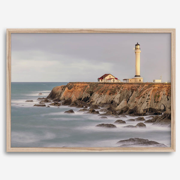 Long exposure fine art photography print of Pigeon Point Lighthouse at sunset. Golden light illuminates the lighthouse and cliffs, while the ocean surf crashes against the rocks in a creamy blur.