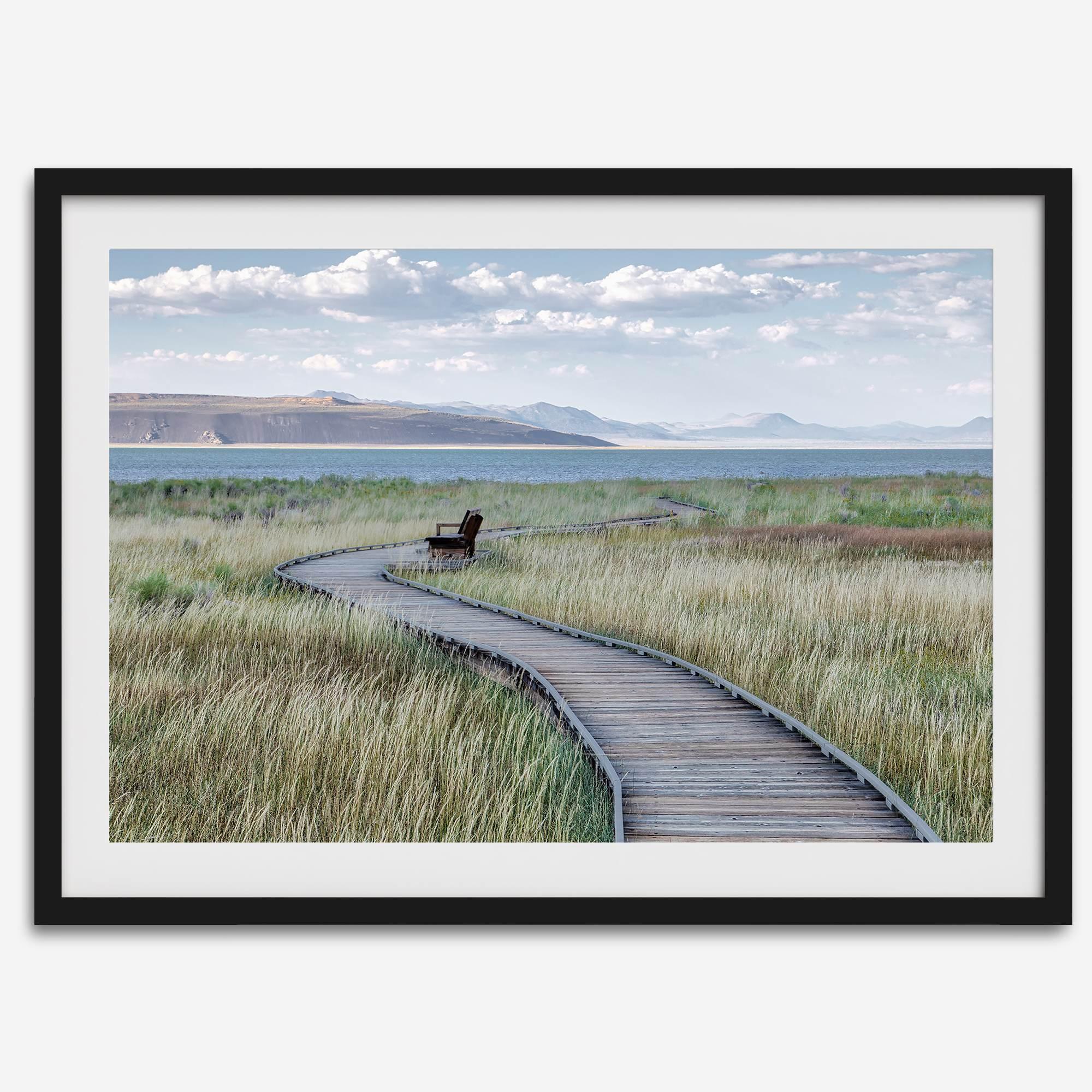 Framed Mono Lake nature photography print featuring a winding boardwalk through tall grasses, leading to a quiet bench beside the lake with mountains in the background.
