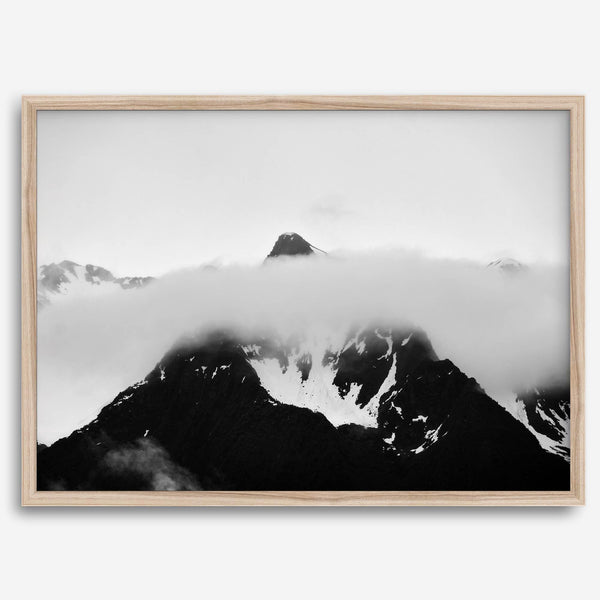 Dramatic black and white landscape of a peak in Alaska, its top rising above a layer of clouds.