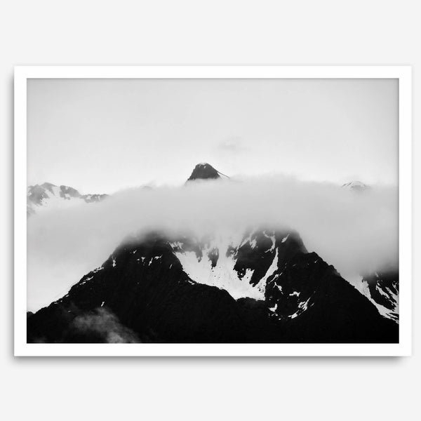 Dramatic black and white landscape of a peak in Alaska, its top rising above a layer of clouds.