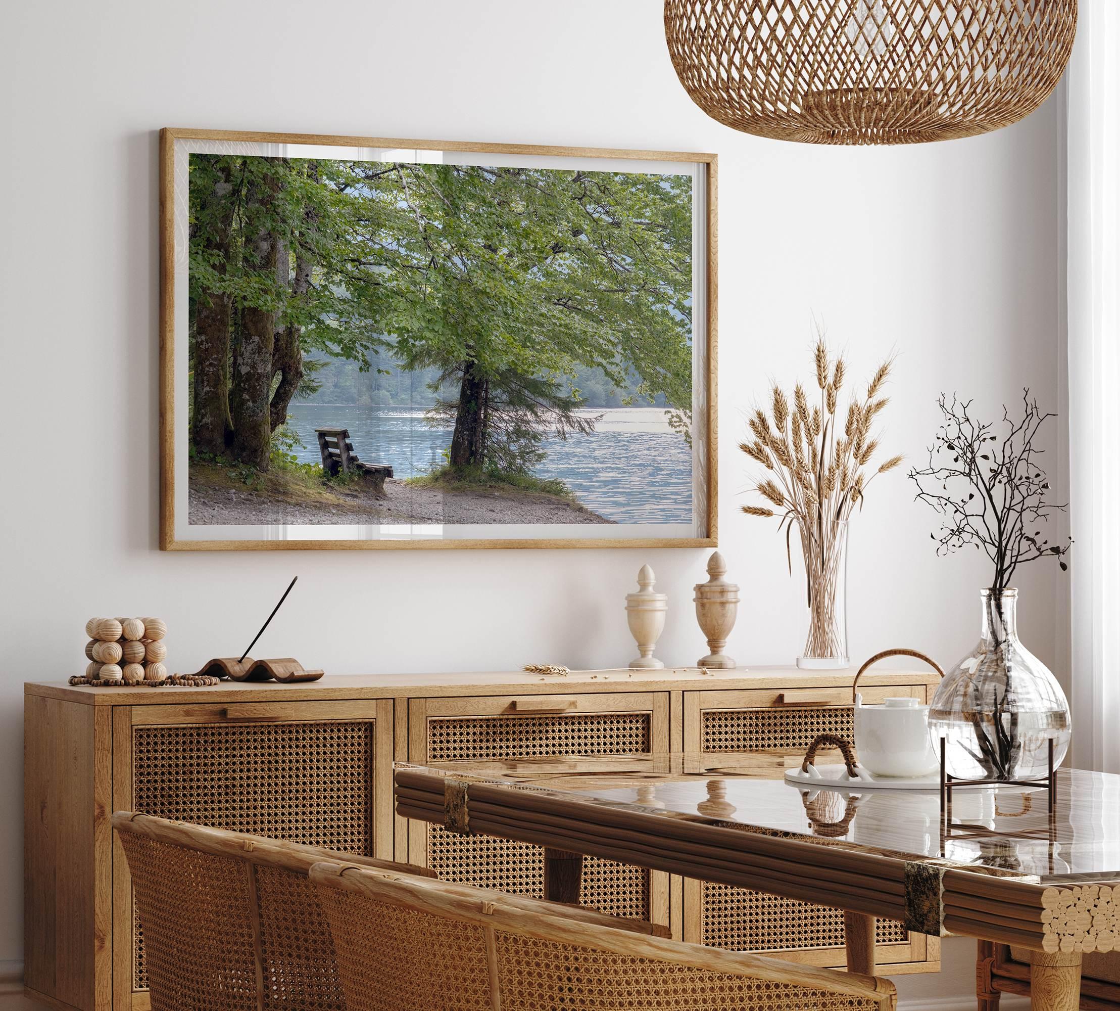 Framed serene lake print showing a bench by the water under lush green trees, with soft sunlight reflected on the calm lake surface.