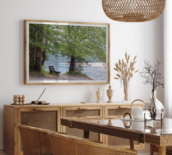Framed serene lake print showing a bench by the water under lush green trees, with soft sunlight reflected on the calm lake surface.