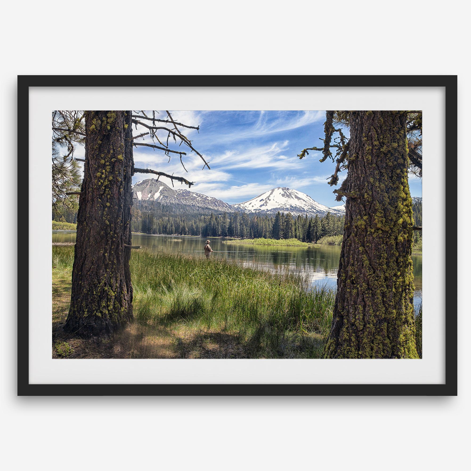 Fisherman at Manzanita Lake beneath snowy mountains and pine forest, photographed as peaceful fishing wall art.