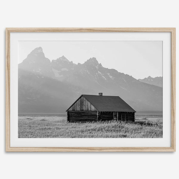 Step into Grand Teton National Park with this fine art black and white mountain print. This western landscape photo showcases a century-old rustic hut at the foot of the snowy, pointy Teton mountains.