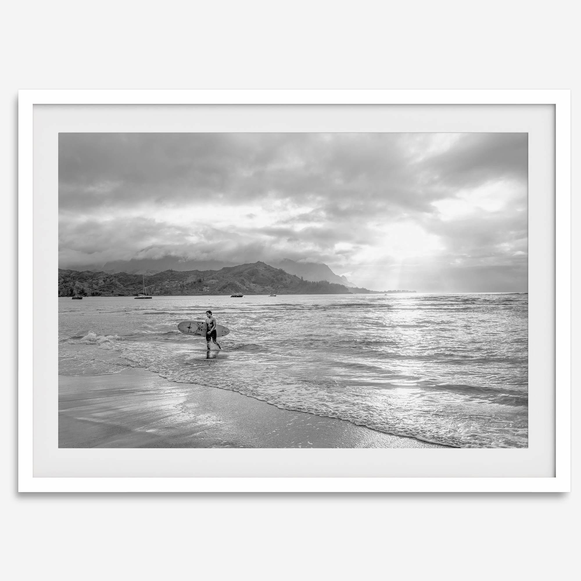 Surfer Wall Art featuring a lone surfer emerging from the ocean at Hanalei Bay in black-and-white photography.
