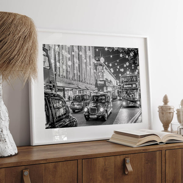 Black and white fine art photography print of a lively London street during Christmas, featuring double-decker buses, black taxis, and festive holiday lights.