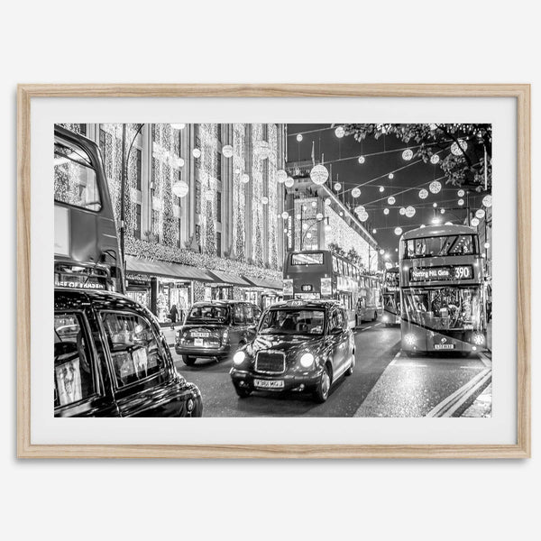 Black and white fine art photography print of a lively London street during Christmas, featuring double-decker buses, black taxis, and festive holiday lights.