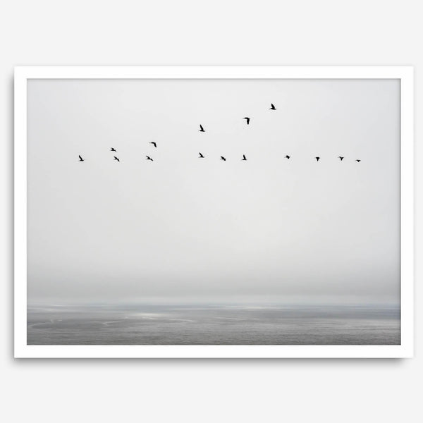 Minimalist seascape fine art print – a flock of birds in flight over a calm, misty ocean with a soft, gray horizon.