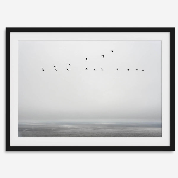 Minimalist seascape fine art print – a flock of birds in flight over a calm, misty ocean with a soft, gray horizon.