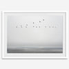 Minimalist seascape fine art print – a flock of birds in flight over a calm, misty ocean with a soft, gray horizon.