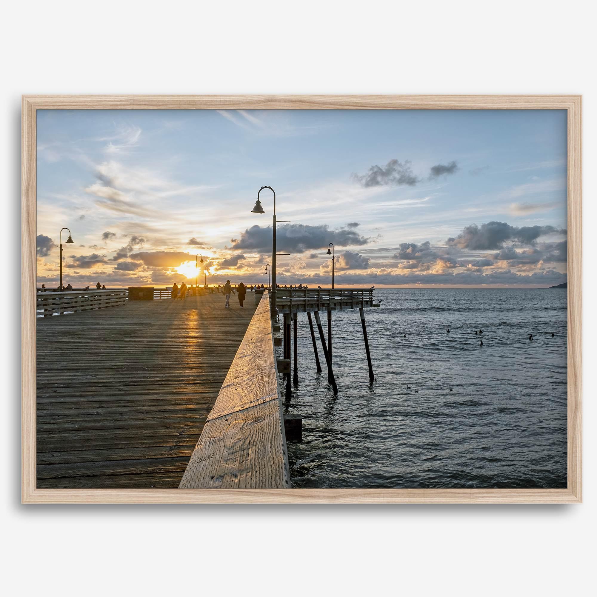 A fine art ocean sunset print featuring Pismo Beach Pier in Sunset with the surfers in the ocean and people enjoying a stroll on the pier.