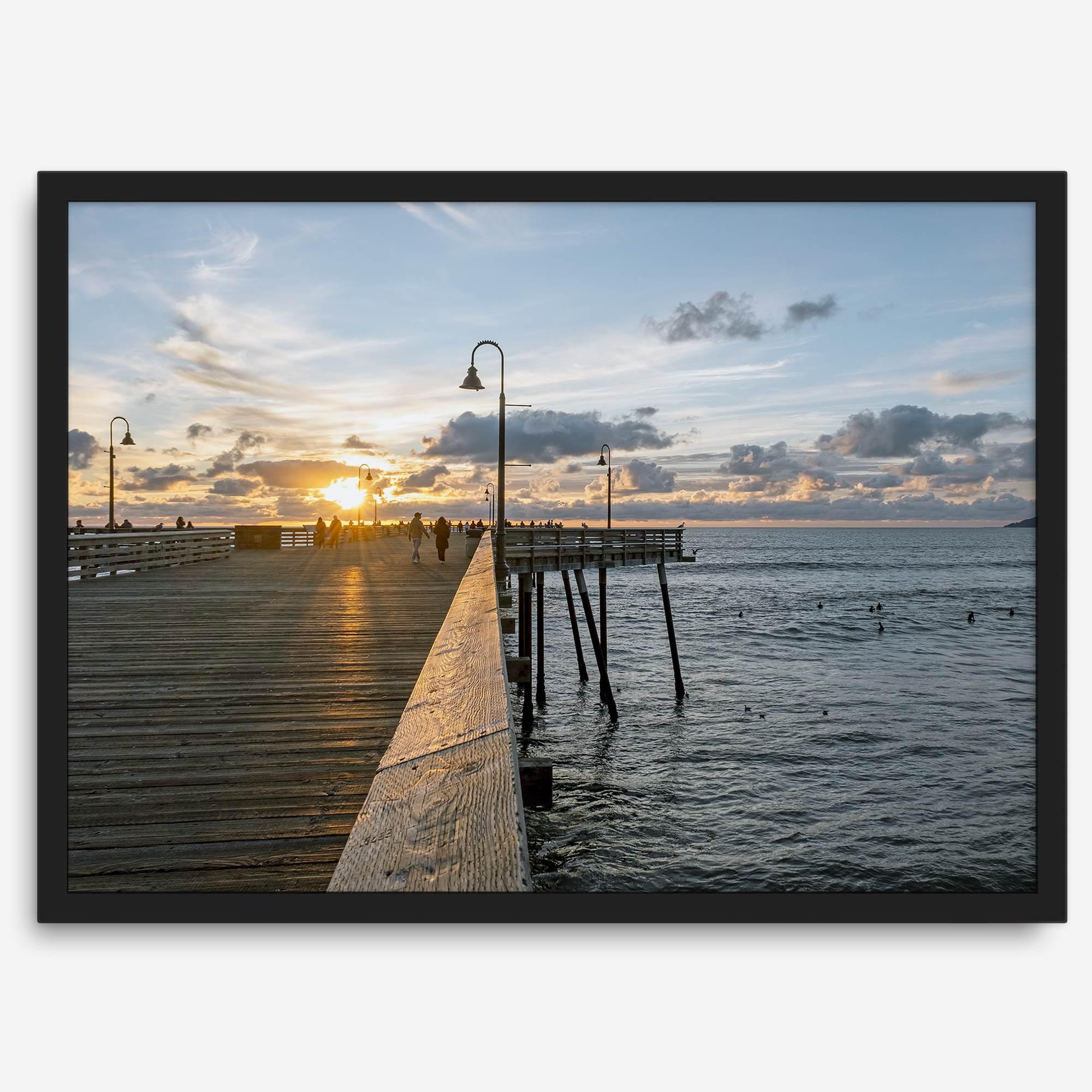 A fine art ocean sunset print featuring Pismo Beach Pier in Sunset with the surfers in the ocean and people enjoying a stroll on the pier.