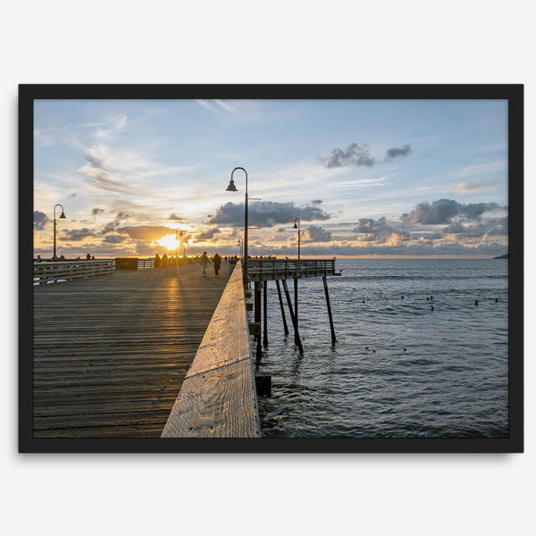 A fine art ocean sunset print featuring Pismo Beach Pier in Sunset with the surfers in the ocean and people enjoying a stroll on the pier.