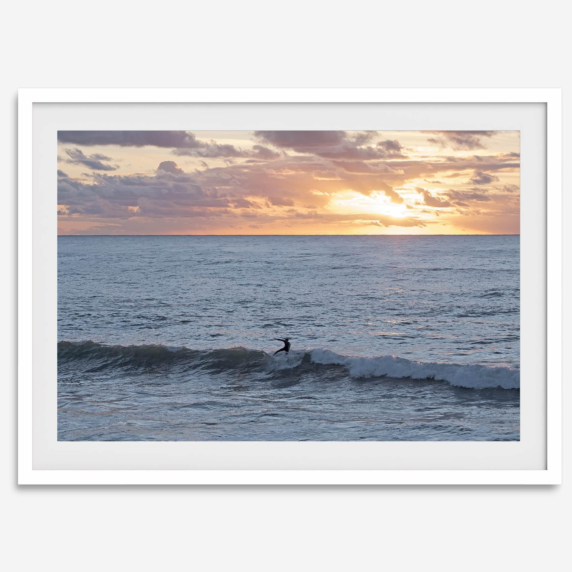 A fine art ocean sunset print showcasing a serene sunset and a lone surfer riding the waves. Taken in Montana De Oro State Park, California.