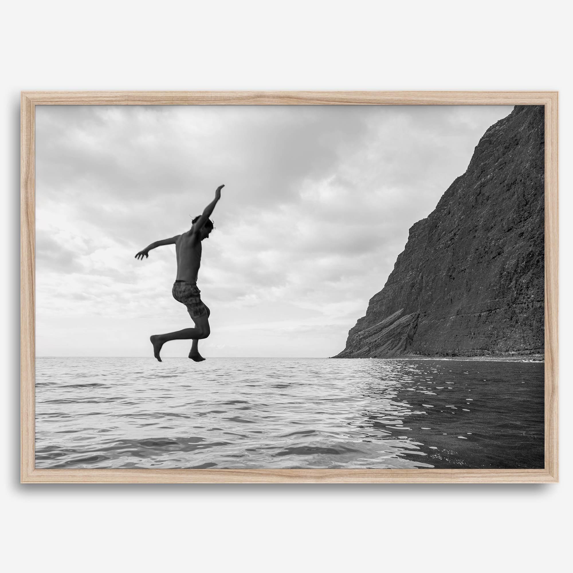 Black and white fine art print of a man mid-jump into the ocean near the cliffs of Na Pali Coast, Kauai.