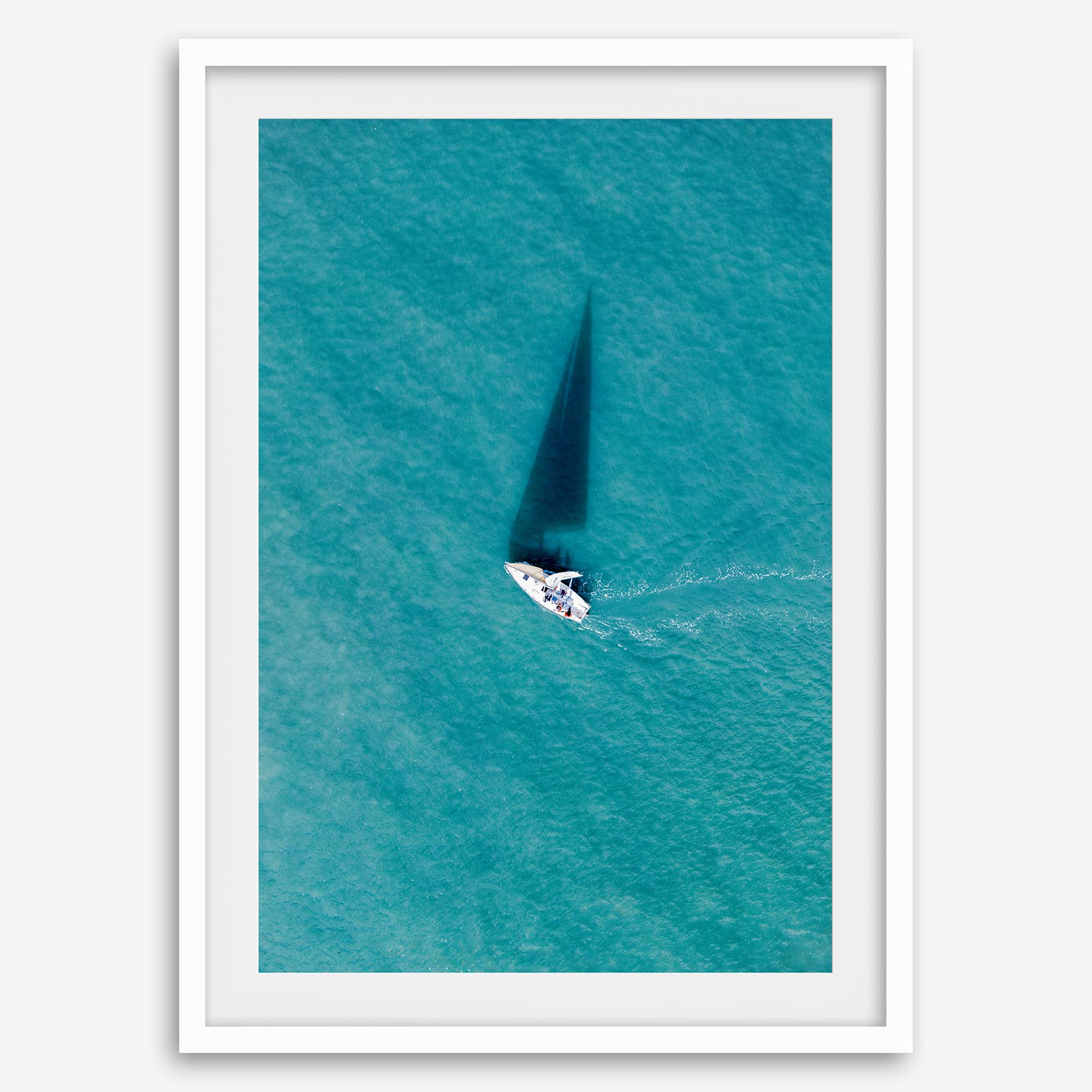 Aerial sailboat photography over turquoise San Francisco Bay near Berkeley, California, with a long sail-shaped shadow across the water.