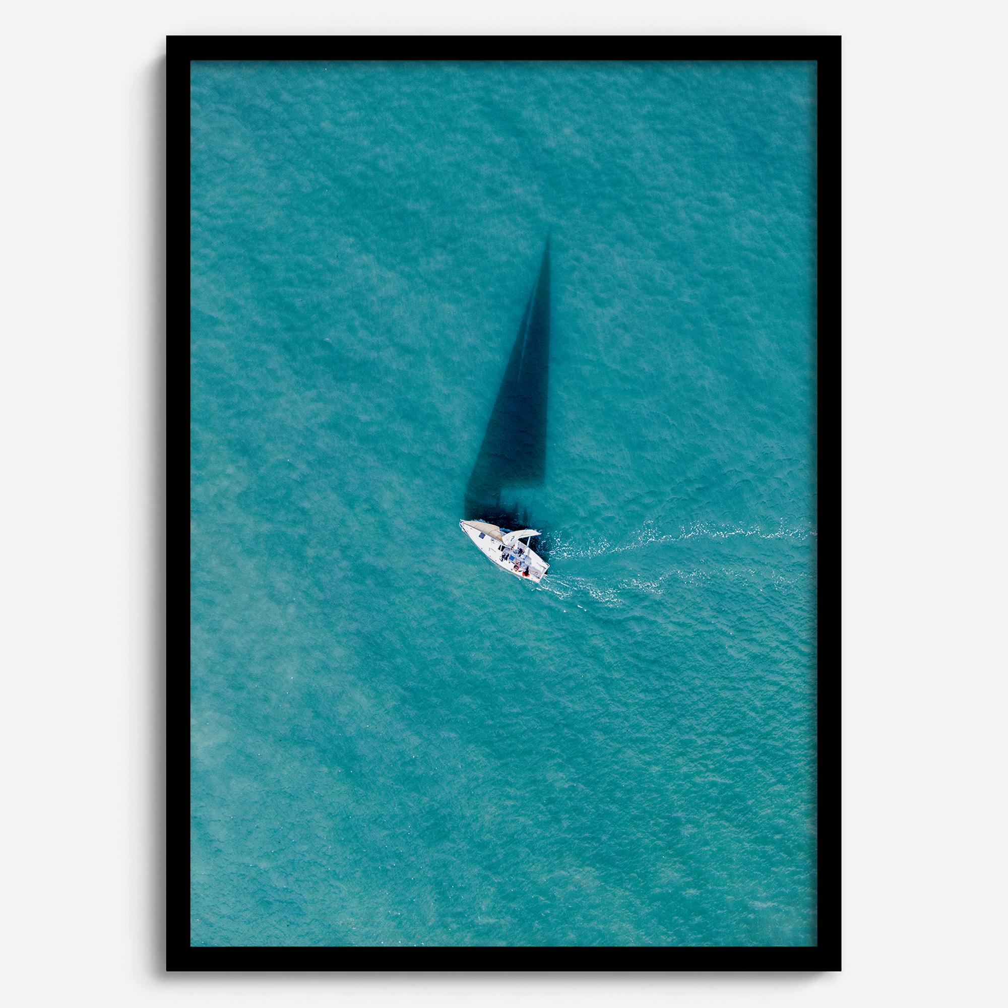 Aerial sailboat photography over turquoise San Francisco Bay near Berkeley, California, with a long sail-shaped shadow across the water.