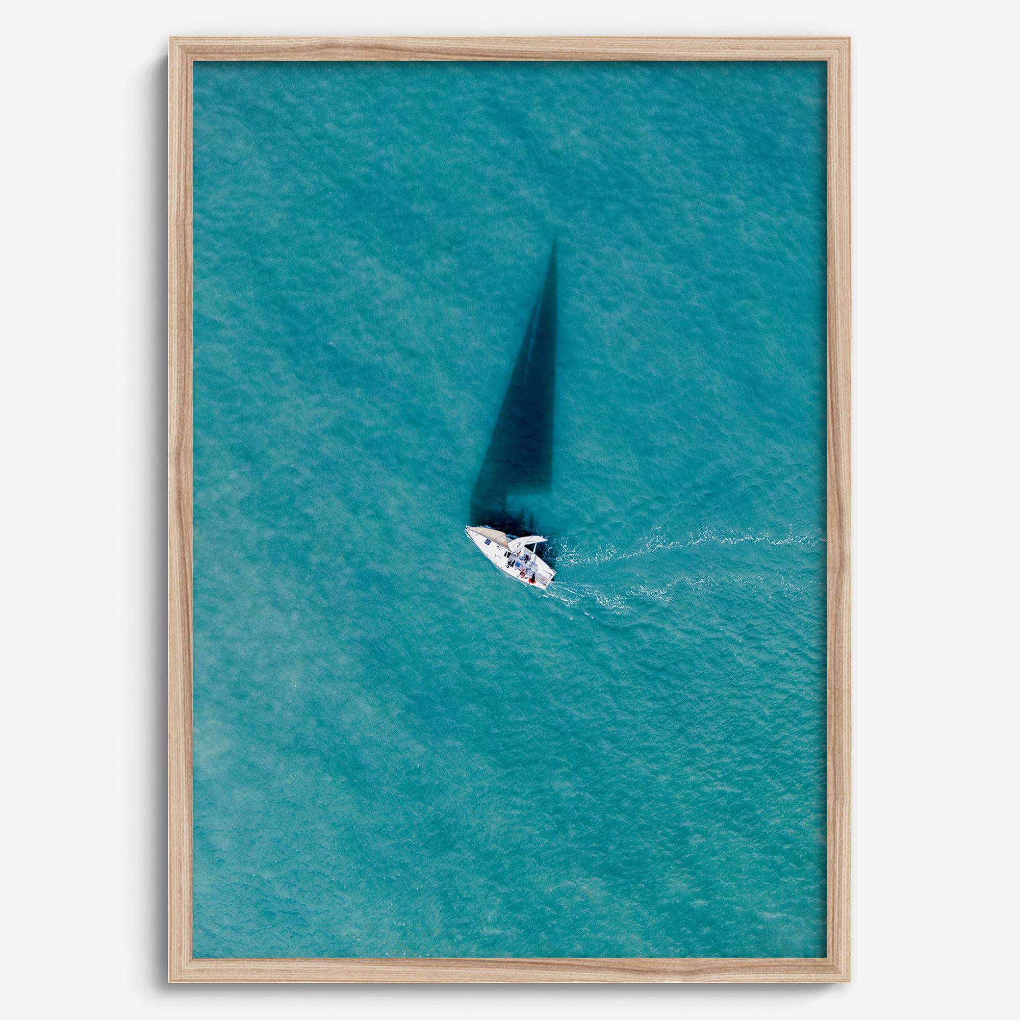 Aerial sailboat photography over turquoise San Francisco Bay near Berkeley, California, with a long sail-shaped shadow across the water.