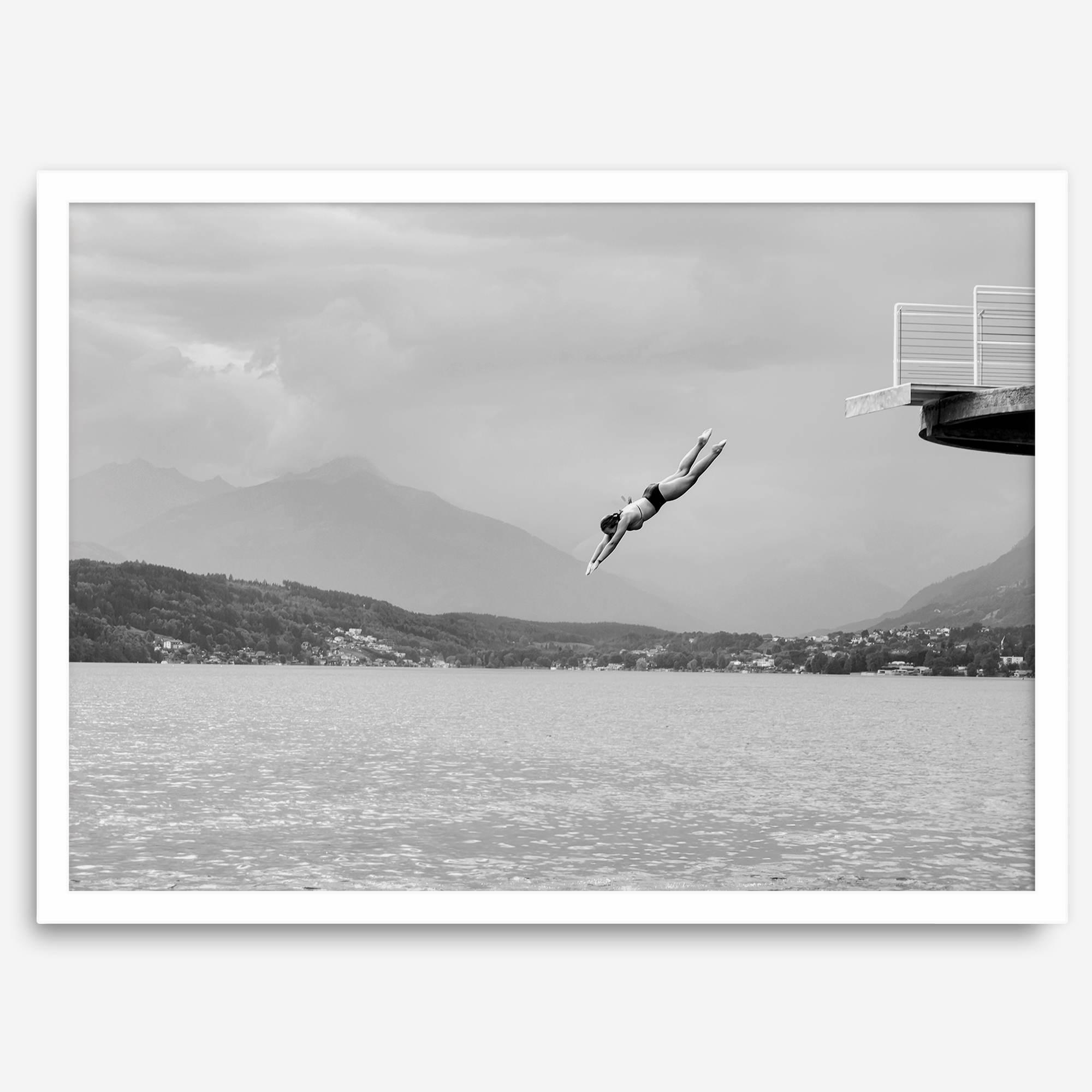 Diver leaping from a platform over a serene Austrian lake, with misty mountains in the background.