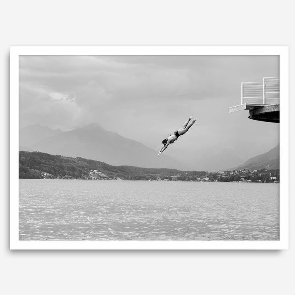 Diver leaping from a platform over a serene Austrian lake, with misty mountains in the background.