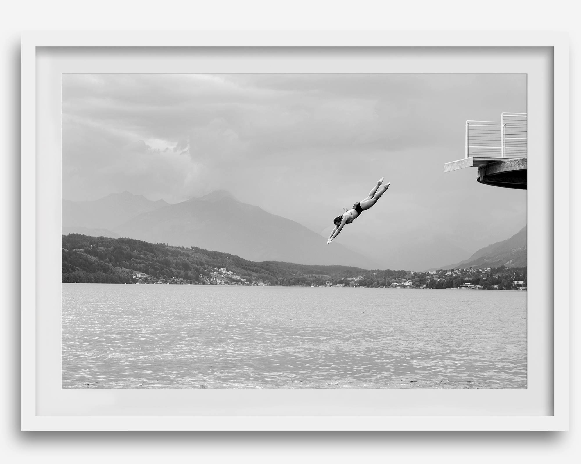 Diver leaping from a platform over a serene Austrian lake, with misty mountains in the background.