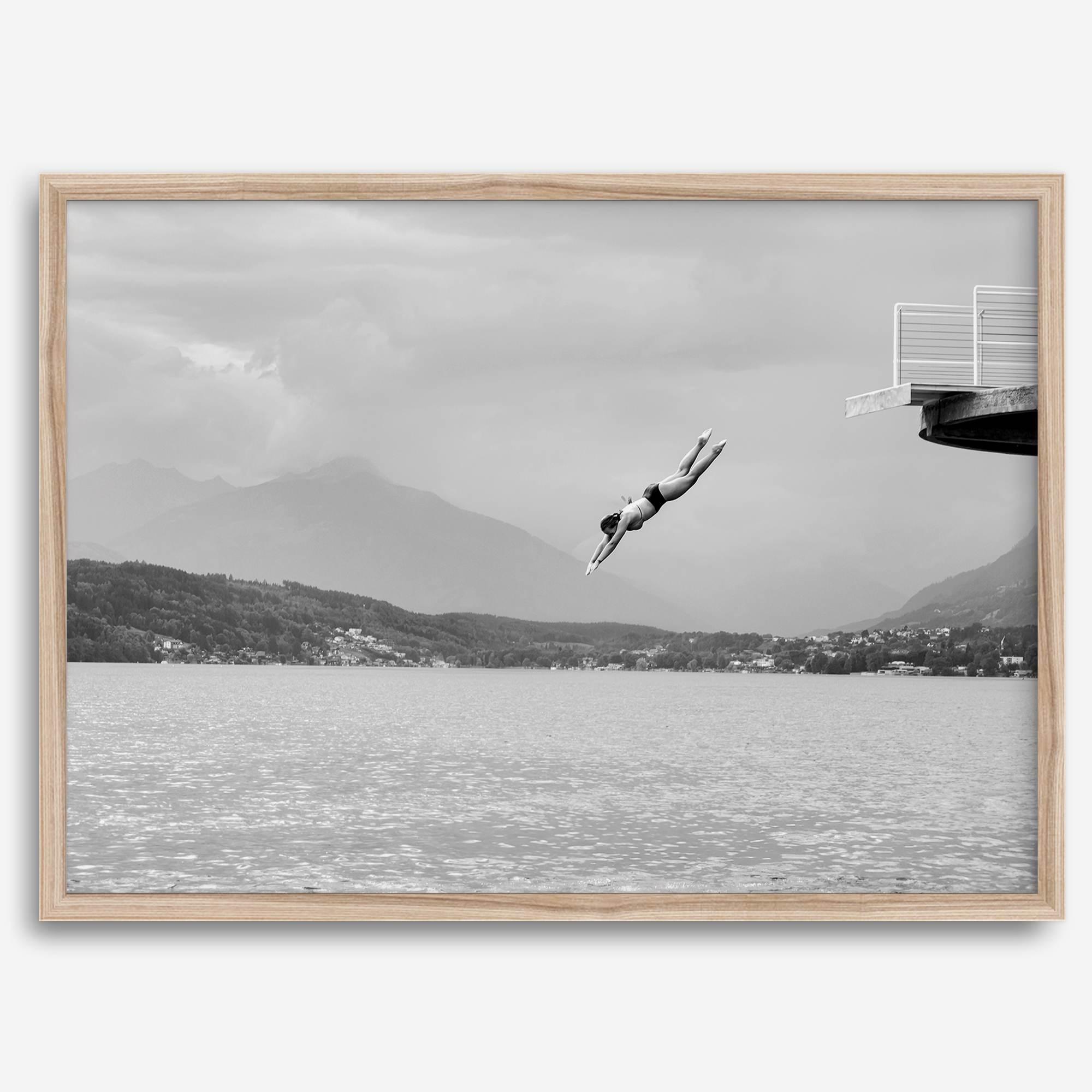 Diver leaping from a platform over a serene Austrian lake, with misty mountains in the background.