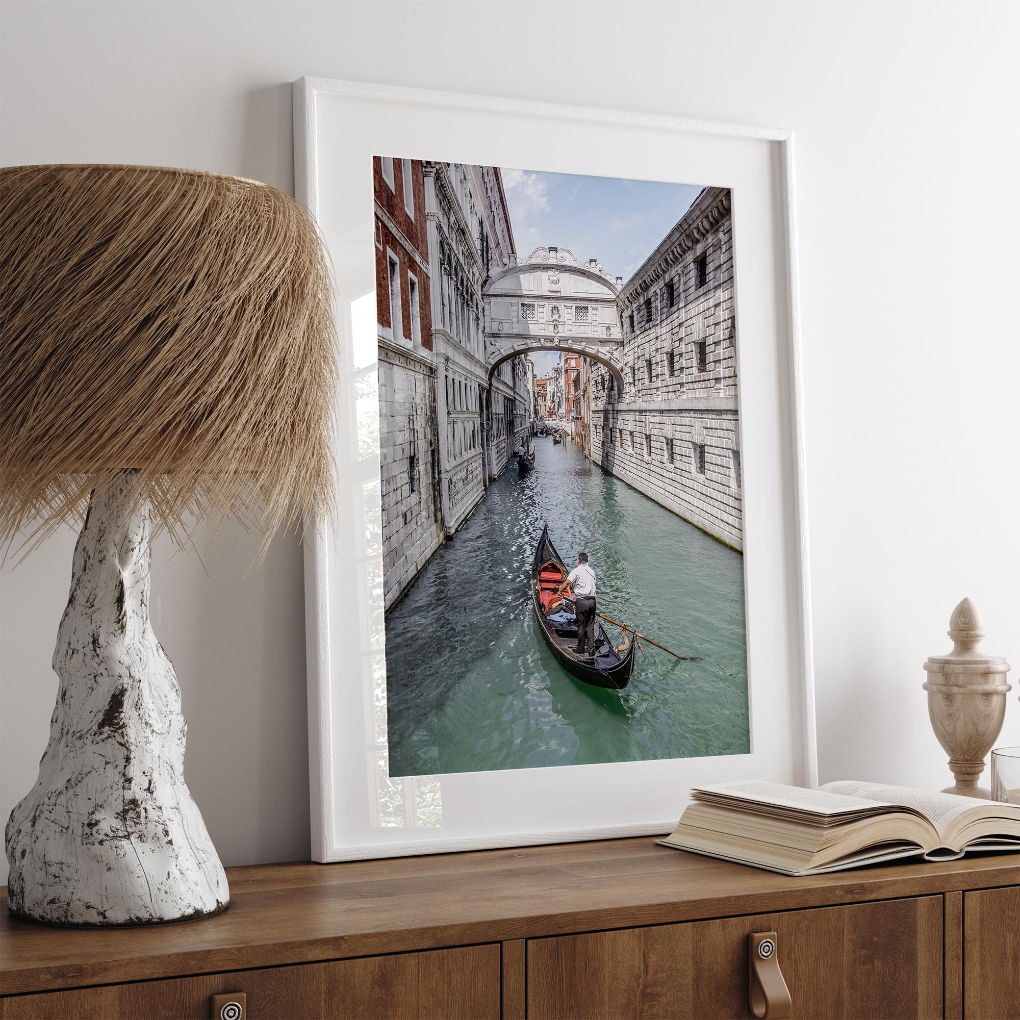 Venice canal photography print featuring a gondola approaching the Bridge of Sighs between historic stone buildings in Venice, Italy.