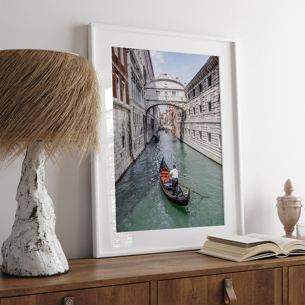 Venice canal photography print featuring a gondola approaching the Bridge of Sighs between historic stone buildings in Venice, Italy.