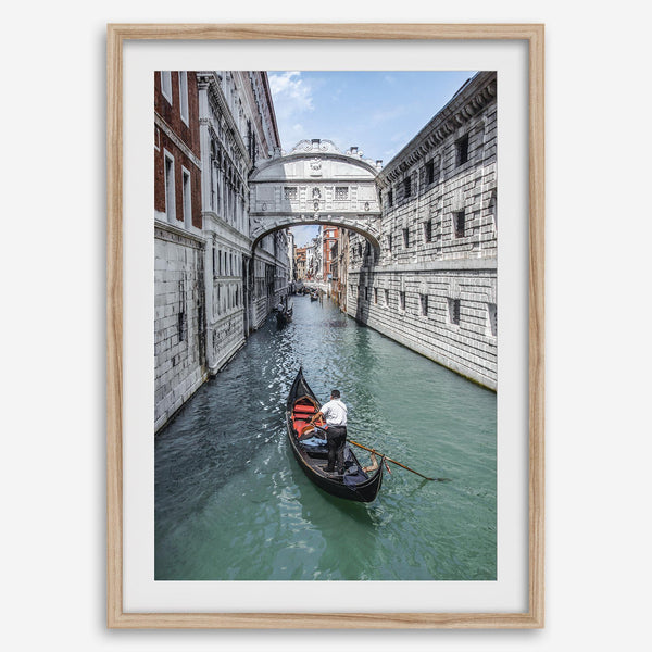 Venice canal photography print featuring a gondola approaching the Bridge of Sighs between historic stone buildings in Venice, Italy.