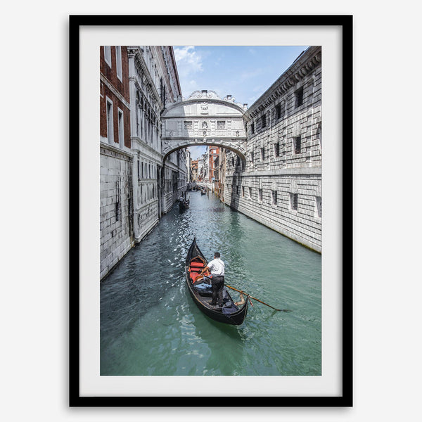 Venice canal photography print featuring a gondola approaching the Bridge of Sighs between historic stone buildings in Venice, Italy.