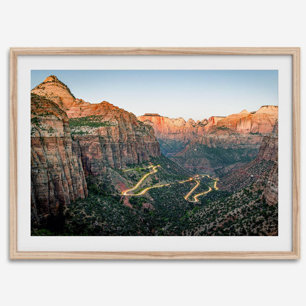 Framed Zion National Park print with winding road illuminated through red cliffs and majestic canyon scenery at dusk.