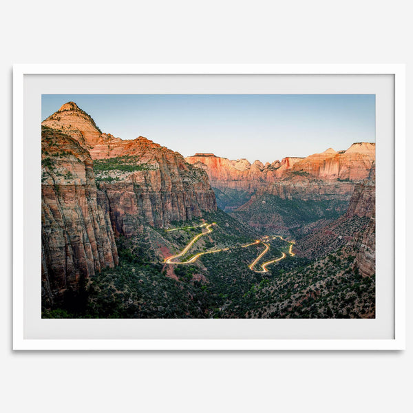 Framed Zion National Park print with winding road illuminated through red cliffs and majestic canyon scenery at dusk.