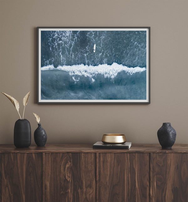 Aerial ocean wall art featuring a lone surfer and a breaking white wave in the deep blue waters of Hanalei Bay.
