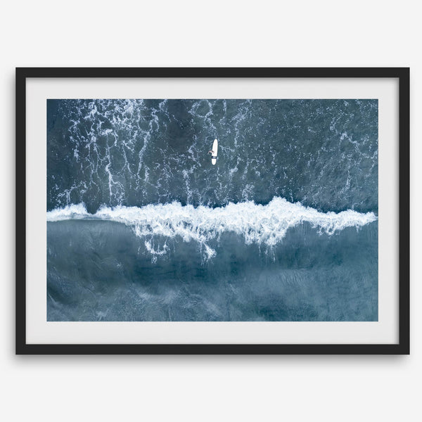 Aerial ocean wall art featuring a lone surfer and a breaking white wave in the deep blue waters of Hanalei Bay.
