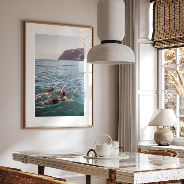 Summer wall art of a coastal Hawaiian landscape with figures swimming in deep blue ocean water.