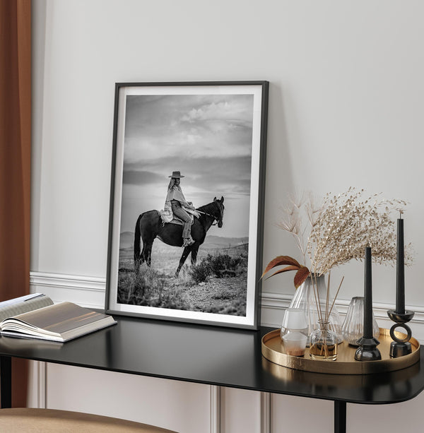 A black and white western rustic wall art - Cowgirl on horseback at sunset in desert landscape