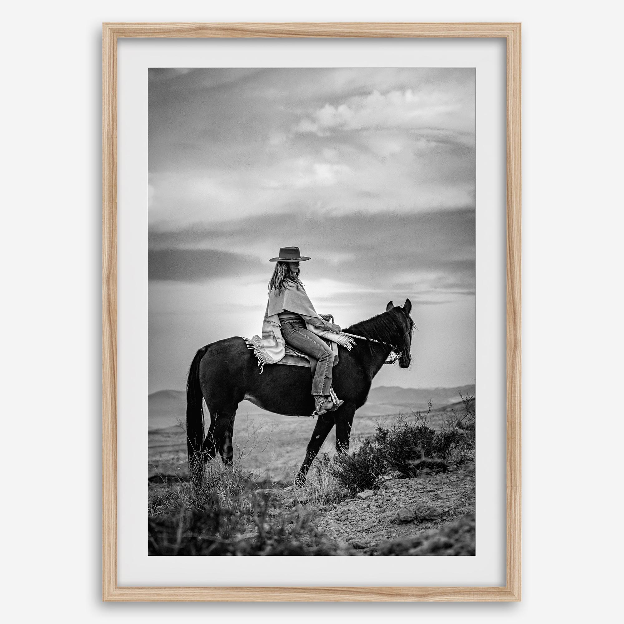 A black and white western rustic wall art - Cowgirl on horseback at sunset in desert landscape