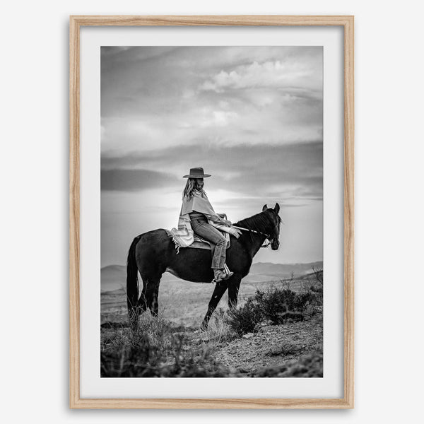 A black and white western rustic wall art - Cowgirl on horseback at sunset in desert landscape